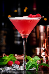 Clover club alcoholic cocktail drink with dry gin, raspberry syrup, lime juice, quail egg white and ice in glass. Black bar counter background, bar tools and bottles