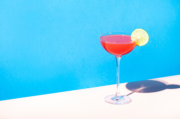 Siesta alcoholic cocktail drink with silver tequila, grapefruit and lime juice, syrup and italian red bitter liqueur, summer blue bright background, hard light and shadows