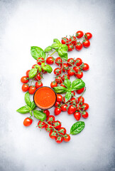 Freshly squeezed tomato juice in a glass and red cherry tomatoes on branches with green basil on gray table, food background, top view