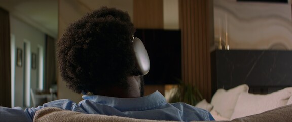 African-American male putting on headphones in his living room, listens to music