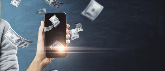 Winning online lottery or on bets on sports concept with woman hand holding smartphone with money rain on dark background