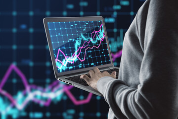 Close up of hacker hands using laptop with glowing forex index chart with grid on dark background. Market, finance and online trading concept.