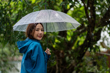 Rainy day asian woman wearing a raincoat outdoors. She is happy.