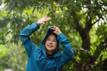 Young Asian woman smiling and wearing a raincoat on a rainy day in the park