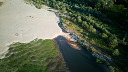 Aerial view of a sandy beach with some green plant, formed as a result of the river drying up during the hot summer, golden hour. 
