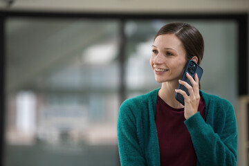 Happy businesswoman standing using a smartphone in a modern office.