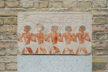 restored painted fragment of a limestone relief depicting Egyptian soldiers and nubian mercenaries...