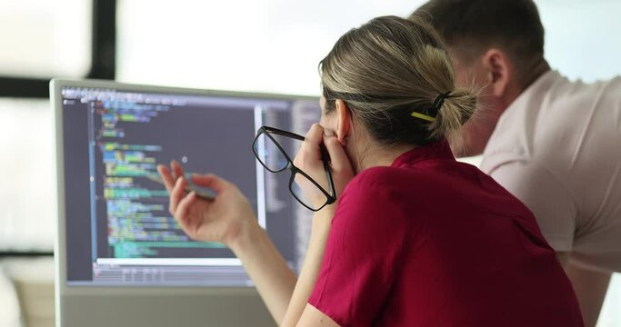 Woman shows program coding on computer monitor to man colleague in office. Partners examine coding errors and bugs on computer screen slow motion
