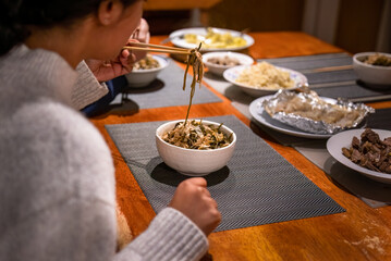 Left-handed woman holding chopsticks and eating dinner. Vegetable and beef dishes on the dinner table.  Home cooking and eating concept.