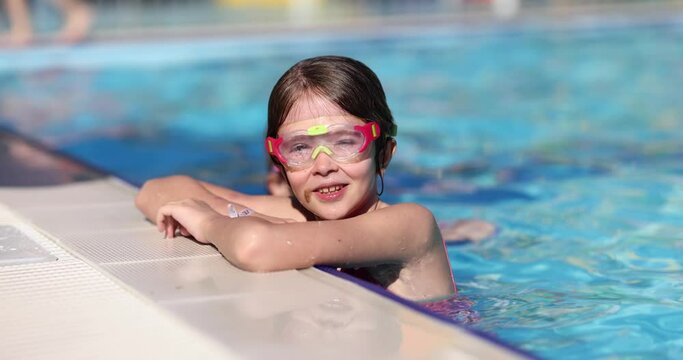 Smiling teenage girl swims in hotel pool wearing goggles. Happy junior schoolgirl enjoys spending time in water during family vacation at exotic resort