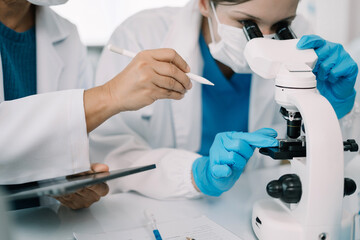 Team of biochemical research scientists working with a microscope for vaccine development in...