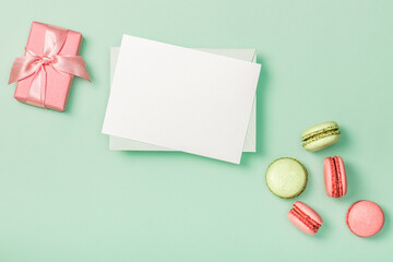 Flat lay composition with blank empty, pink gift box and colorful macaroons on light green background. Greeting card. Invitation.