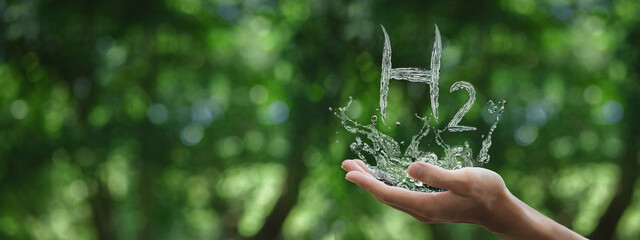 Human hand splashing water with the word H2 on a green background. Clean energy generation concept with hydrogen gas for sustainable environmental investment.