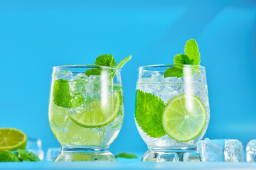 Two glasses of mojito cocktail with ice cubes on a blue background. Low angle view. Studio shot.