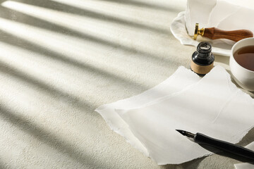 Sheets of paper, stamp, ink bottle and pen, cup of tea on light background, space for text