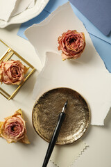 Pieces of paper, roses and golden plate on white background, top view