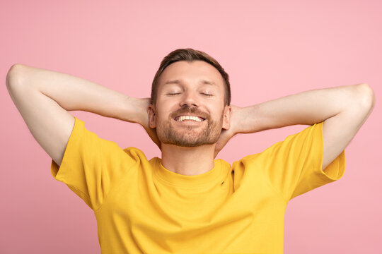 Happy man feel freedom good mood arms relaxed over head with white teeth, satisfied closed eyes isolated on pink studio blank wall. Cheerful guy enjoy vacation completed tasks on copy space background