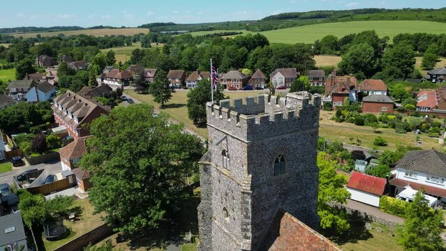A relaxed arc-shot of Chartham, focused on the tower of St Mary's church, flying the union flag.