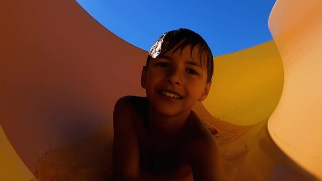 The cheerful little boyvis riding down an orange slide 