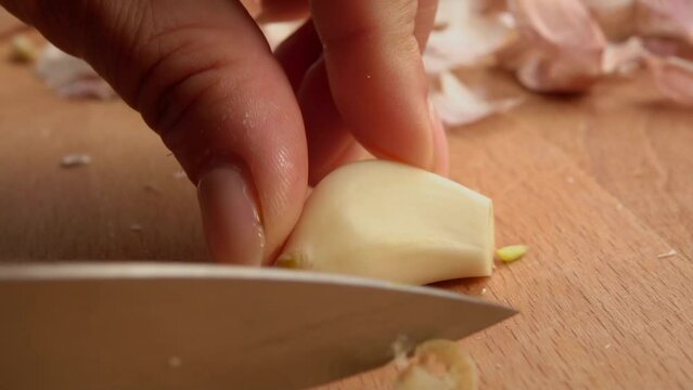 A knife cuts a clove of garlic into long cloves