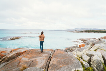 Wide shot of Woman standing on Rocks at Bay of Fires near Suicide Beach via the Gardens Road, in Tasmania, North East Tasmania, Australia