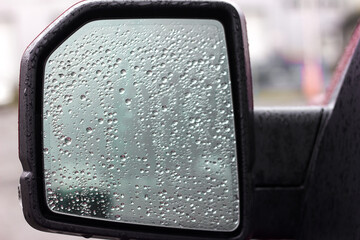 Raindrops on the side mirror of the car on the driver's side, the danger of driving in a car in rainy weather