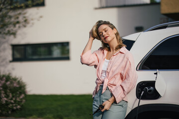 Young woman charging her electric car in home, sustainable and economic transportation concept.