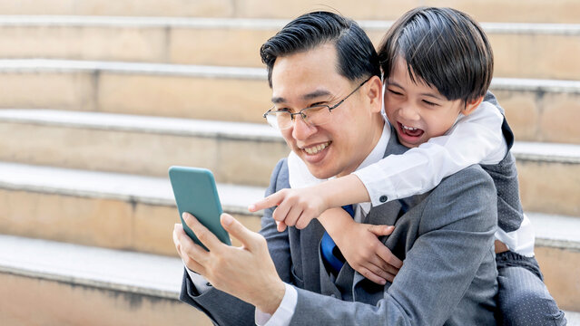 Father and son playing  smart phone together on business district urban, Dad and Son happy Asian family concept