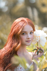 Close-up portrait of a red-haired girl with peonies in a summer garden