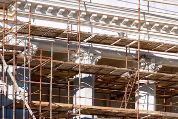 Building facade renovation, scaffolding. Columns restoration of an old historic building. Reconstruction. Facade renovation of historical building with bas-relief stucco and decorative details.