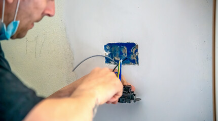 Electrician mounts an electrical outlet to the wall, connecting cables