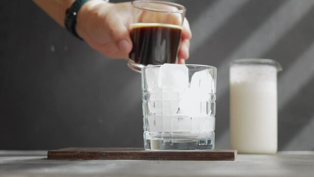 Male hand pouring espresso coffee drink in to a glass with ice cubes, process of making cold iced latte coffee