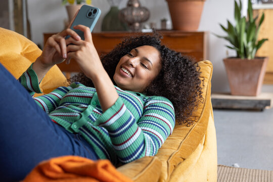 Young adult woman messaging friend lying on sofa 