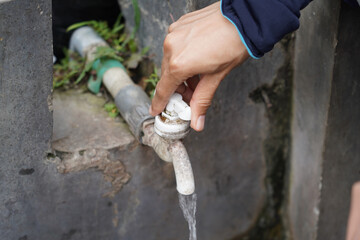Woman's hand closing an abandoned and worn outdoor water faucet to stop the water.