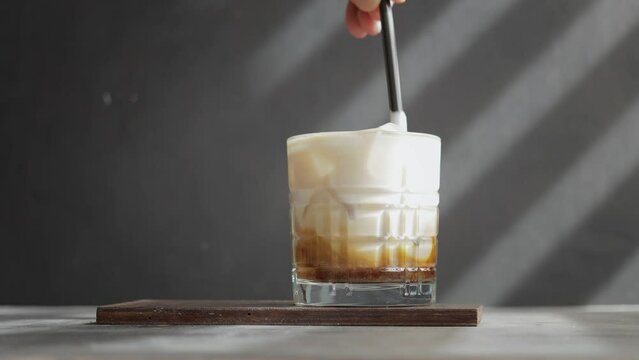 Male hand with a straw mixing ice latte coffee in a glass, whipped milk with espresso and ice cubes