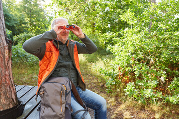 Elderly man bird watching through binoculars in forest