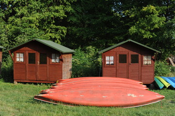 Kayaks stacked in a row on a green meadow with wooden summer houses on a sunny summer day
