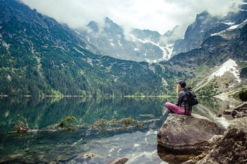 A young girl sitting on a stone by a mountain lake admires the views. Morskie Oko lake, Poland. - obrazy, fototapety, plakaty