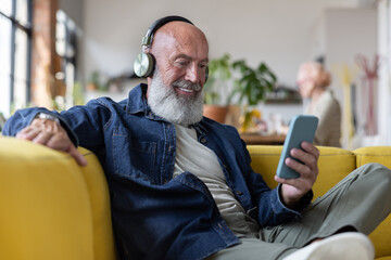 Cool senior man at home using a smartphone with headphones to listen to music