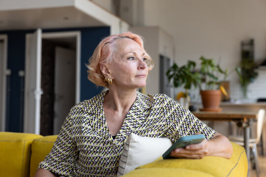 Trendy senior woman at home alone looking out of window thinking