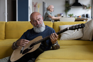 Trendy senior man playing acoustic guitar at home