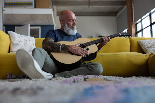 Trendy senior man playing acoustic guitar at home