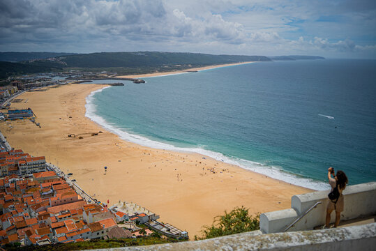 Tourist woman is taking a picture with her phone of a beautiful endless beach in  Nazare Beach in Portugal