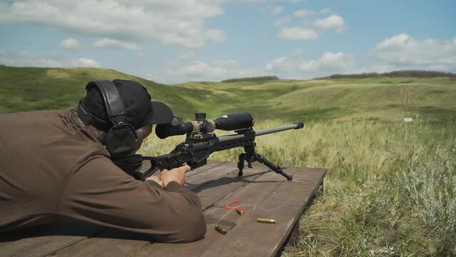 A shooter in a black cap takes aim and shoots a rifle at the target