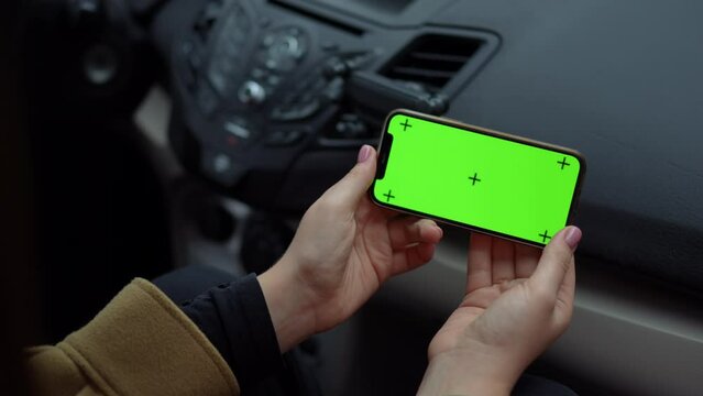 Close-up green screen smartphone in female Caucasian hands high angle view. Closeup unrecognizable young woman with chromakey phone sitting in car