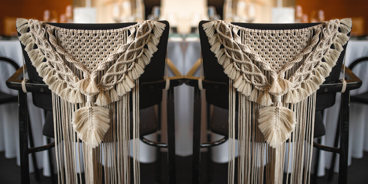 Wedding table in boho style decorated. Two chairs for the wedding couple from behind with complex macrame decoration.