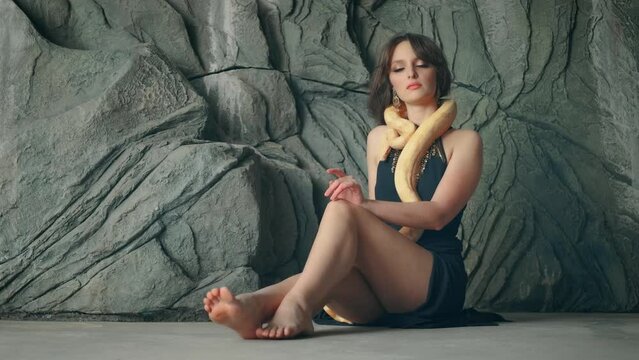 fantasy woman queen of snakes. Girl vampire fashion model posing with yellow tiger python snake animal. Beauty face. Lady love pet anaconda crawls over neck body face. black sexy dress. 4k art footage