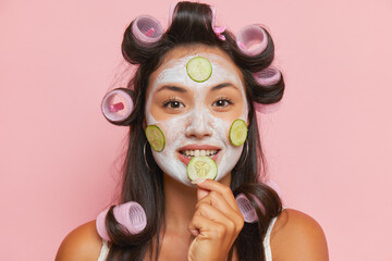 Face portrait of cute girl with curlers on long black hair, cosmetic procedures, cream mask with...