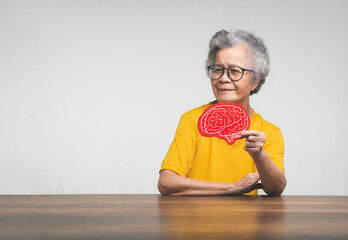 Senior woman holding a brain symbol and looking at the camera with a smile while sitting at the...