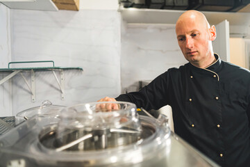 Pastry chef at work. Bald caucasian man attentively oversees the operation of professional ice cream mixer. High quality photo